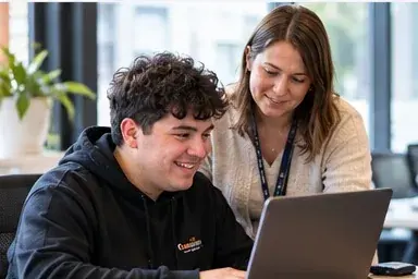 A young man working on a laptop with a mentor beside him