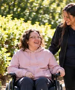 A smiling woman in a wheelchair enjoying a garden walk with a companion
