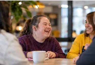 A young woman laughing with friends over coffee at a café